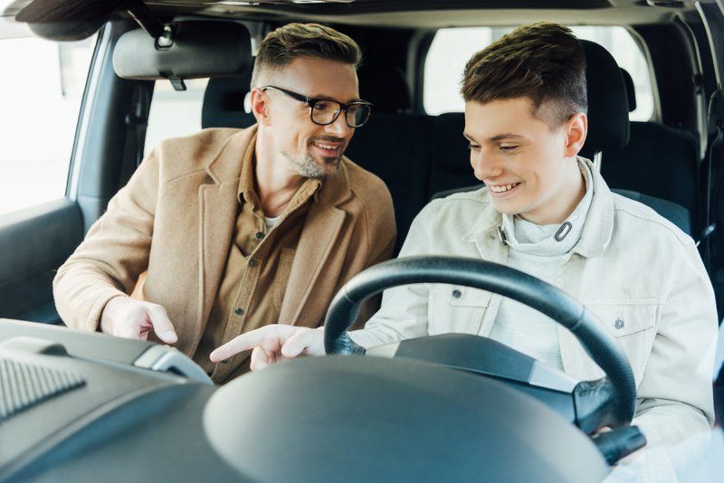 smiling handsome father teaching teen son driving car
